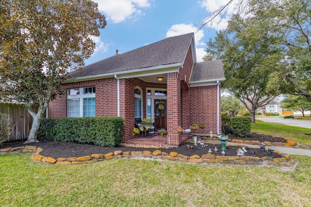 view of front of house featuring a shingled roof, brick siding, fence, and a front lawn