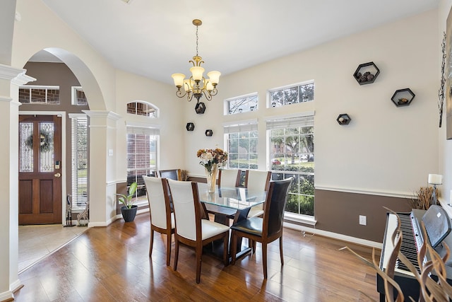 dining area with decorative columns, arched walkways, baseboards, wood-type flooring, and an inviting chandelier