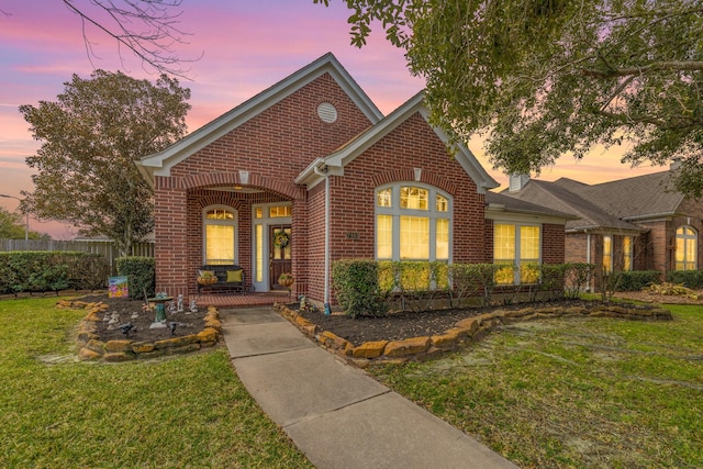 view of front of property with covered porch, brick siding, a yard, and fence