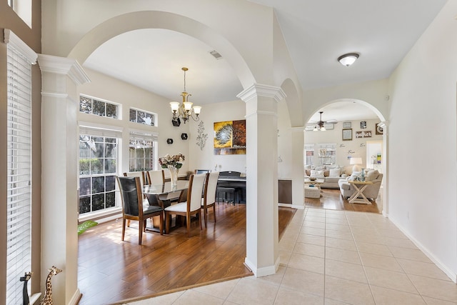 dining area featuring light tile patterned floors, arched walkways, ceiling fan with notable chandelier, baseboards, and decorative columns