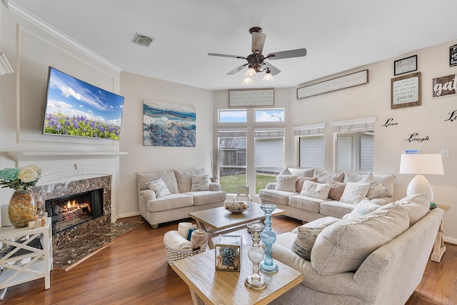 living area with baseboards, visible vents, ceiling fan, wood finished floors, and a high end fireplace