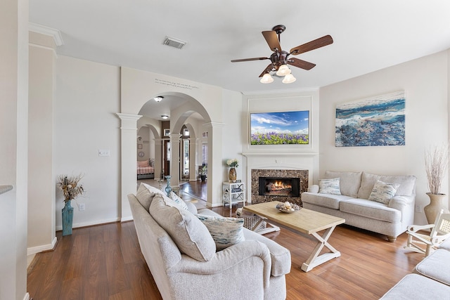 living area featuring arched walkways, visible vents, a high end fireplace, wood finished floors, and baseboards