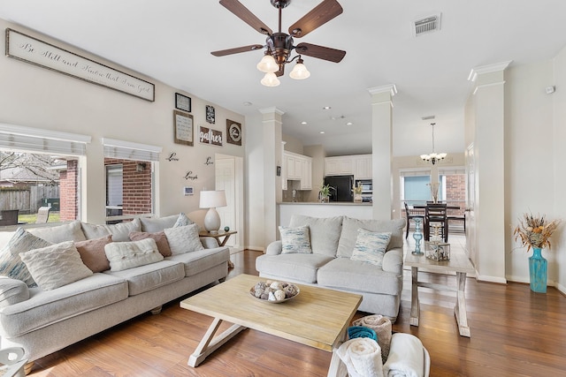 living area featuring decorative columns, visible vents, wood finished floors, and ceiling fan with notable chandelier