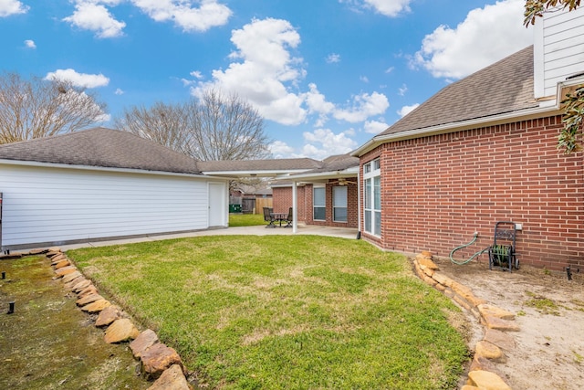 rear view of property featuring a shingled roof, a lawn, a patio, and brick siding