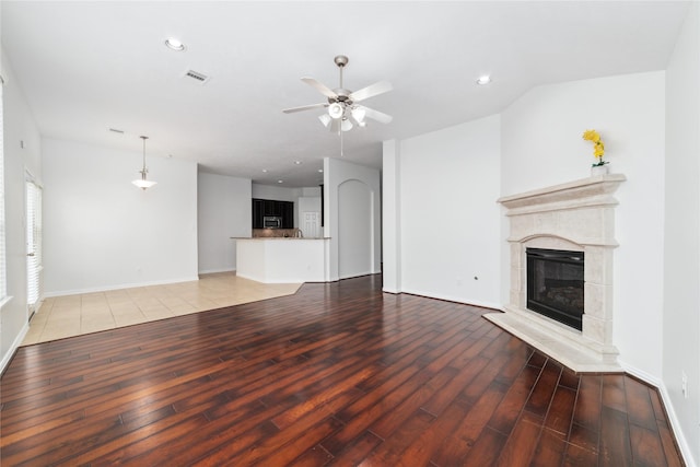 unfurnished living room featuring visible vents, a premium fireplace, light wood-style floors, a ceiling fan, and baseboards