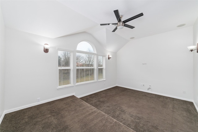 empty room with lofted ceiling, ceiling fan, baseboards, and dark colored carpet