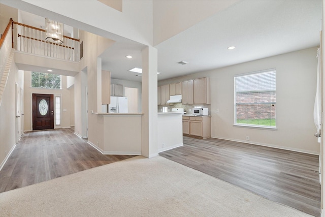 foyer with baseboards, a towering ceiling, an inviting chandelier, light wood-style floors, and recessed lighting