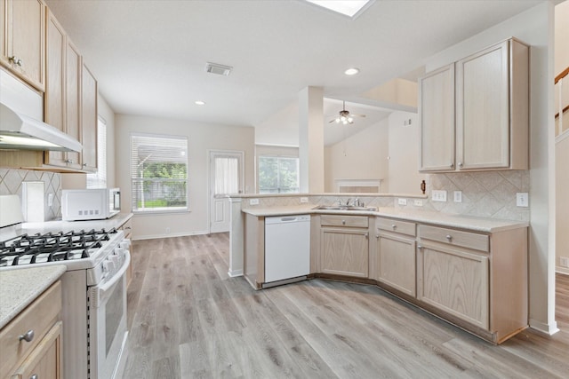 kitchen with a peninsula, white appliances, a sink, light countertops, and light wood-type flooring