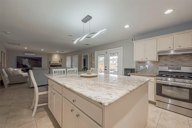 kitchen featuring light tile patterned floors, under cabinet range hood, a kitchen island, stainless steel range with gas cooktop, and tasteful backsplash