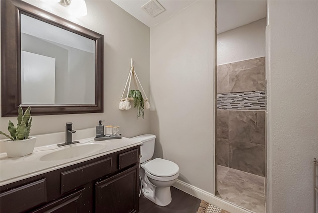 bathroom featuring visible vents, toilet, a tile shower, vanity, and wood finished floors