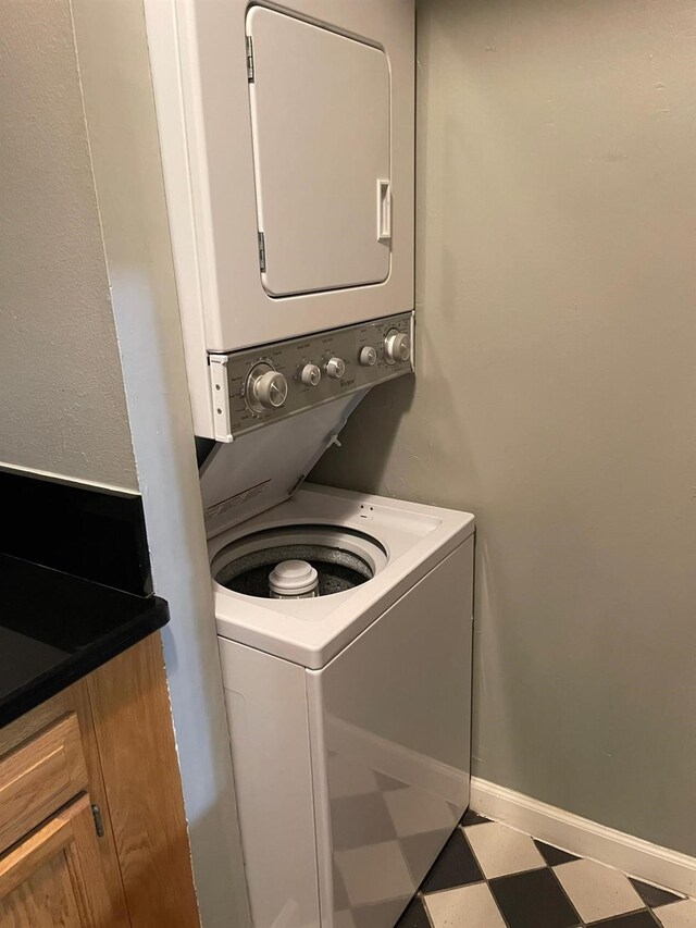 clothes washing area featuring baseboards, stacked washing maching and dryer, and tile patterned floors