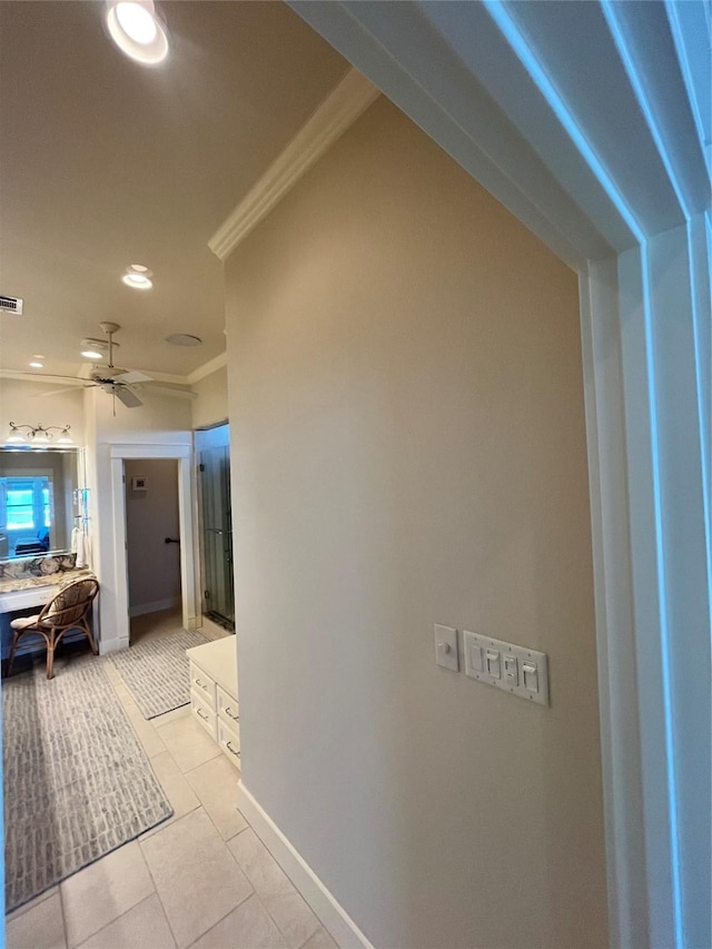 hallway with light tile patterned floors, baseboards, visible vents, and ornamental molding