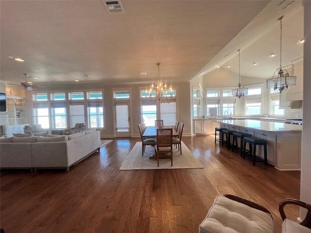 dining space featuring dark wood-style flooring, visible vents, a textured ceiling, baseboards, and ceiling fan with notable chandelier