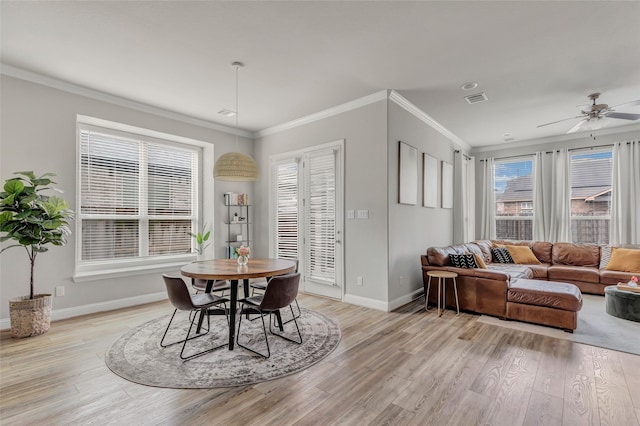 dining area featuring visible vents, light wood-style flooring, ornamental molding, a ceiling fan, and baseboards