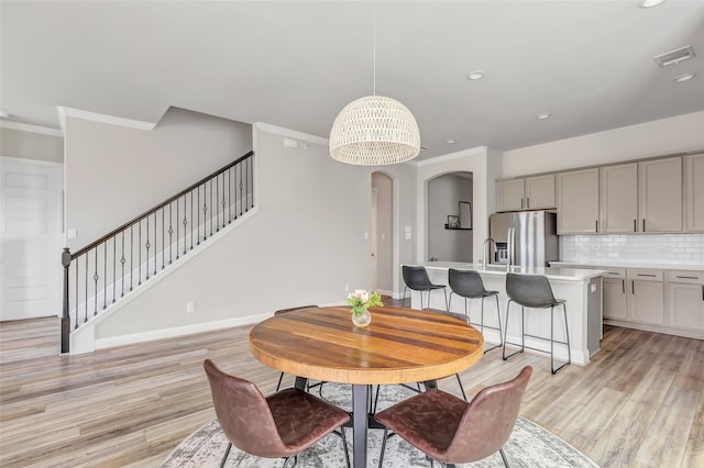 dining space with light wood-style floors, baseboards, visible vents, and ornamental molding