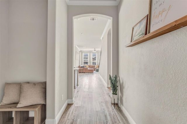 hall with arched walkways, visible vents, ornamental molding, light wood-type flooring, and baseboards