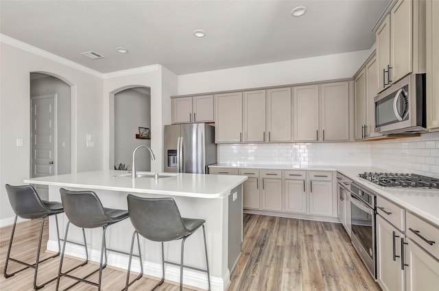 kitchen with stainless steel appliances, a sink, gray cabinets, a kitchen bar, and a center island with sink