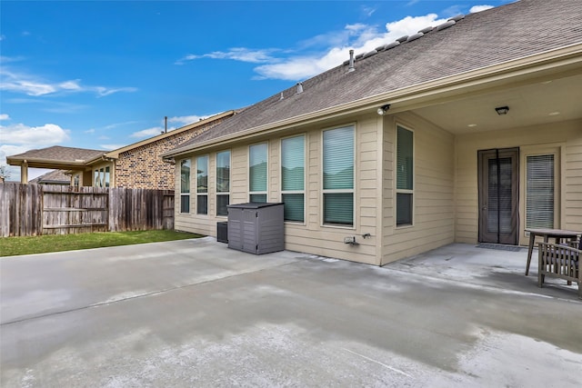 rear view of property featuring roof with shingles, fence, and a patio