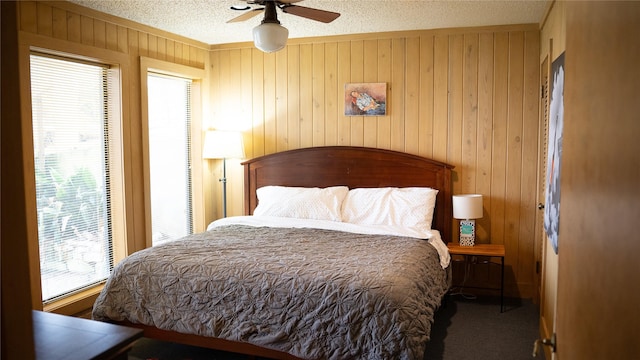 bedroom with wooden walls, carpet, ceiling fan, and a textured ceiling