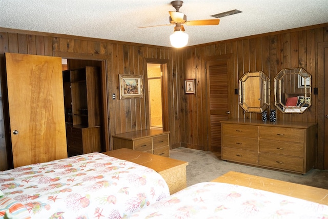 bedroom with a textured ceiling, light colored carpet, wooden walls, visible vents, and ornamental molding