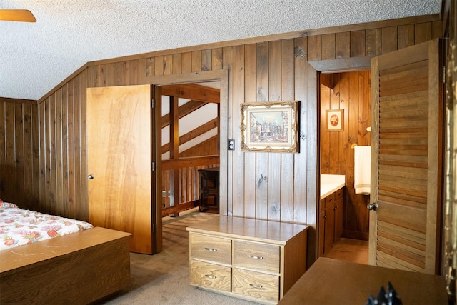 bedroom featuring wooden walls, vaulted ceiling, a textured ceiling, and light colored carpet