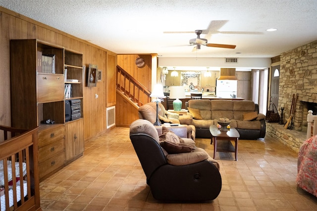 living room featuring visible vents, stairs, a textured ceiling, wood walls, and a fireplace