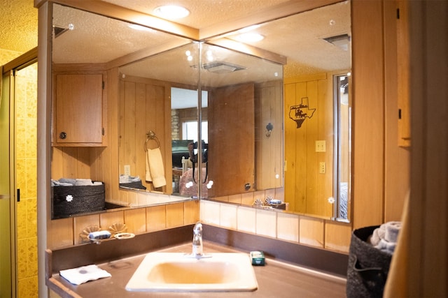 bathroom with a textured ceiling, a sink, visible vents, and wooden walls