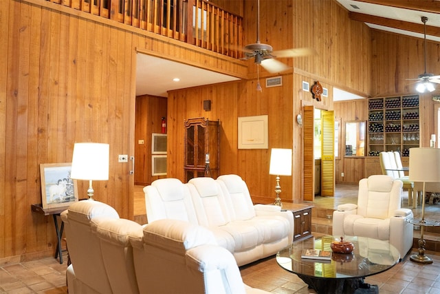 living area featuring wood walls, a towering ceiling, visible vents, and a ceiling fan