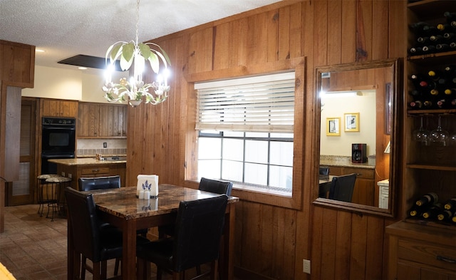 dining area featuring a textured ceiling, wooden walls, and a notable chandelier