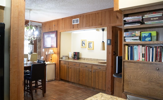 kitchen featuring light countertops, visible vents, brown cabinetry, wooden walls, and a textured ceiling