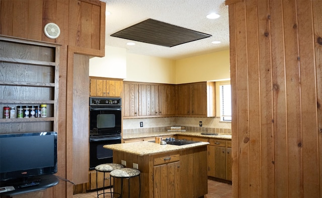 kitchen featuring black appliances, brown cabinets, a textured ceiling, and a center island