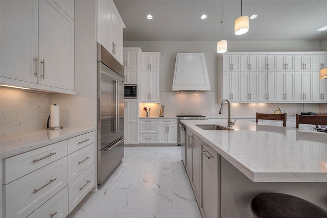 kitchen with marble finish floor, white cabinetry, a sink, built in appliances, and exhaust hood