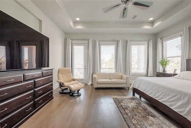 bedroom featuring wood finished floors, multiple windows, a raised ceiling, and visible vents