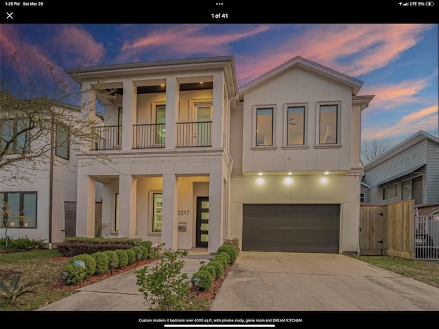 view of front of home with concrete driveway, stucco siding, fence, an attached garage, and a balcony