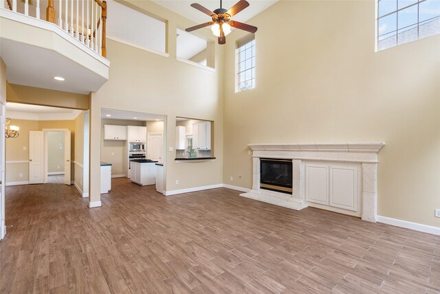 unfurnished living room featuring light wood-type flooring, baseboards, ceiling fan with notable chandelier, and a glass covered fireplace