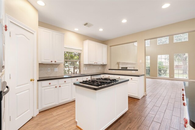 kitchen with light wood-style flooring, a sink, visible vents, backsplash, and dark countertops