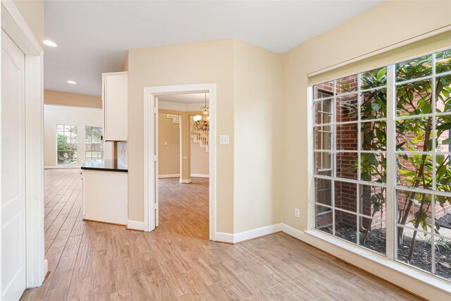 empty room featuring light wood-style flooring, baseboards, a notable chandelier, and recessed lighting