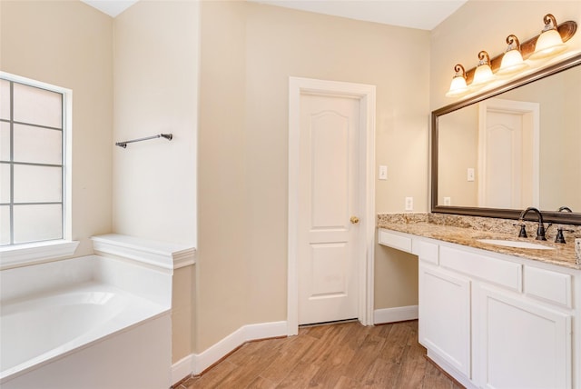 bathroom with a garden tub, vanity, baseboards, and wood finished floors