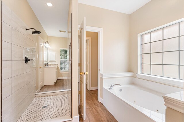 bathroom with wood finished floors, vanity, baseboards, a tub with jets, and a stall shower