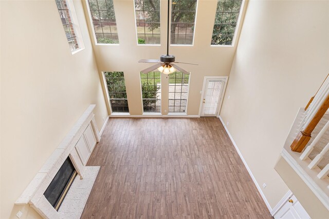 unfurnished living room featuring stairs, a high ceiling, a fireplace, and wood finished floors