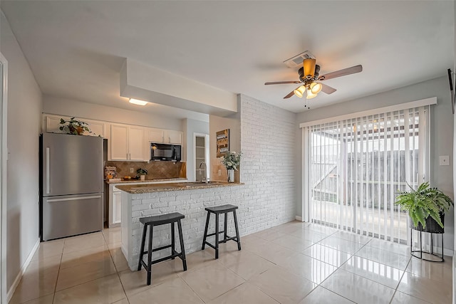 kitchen featuring black microwave, light tile patterned floors, a breakfast bar area, white cabinets, and freestanding refrigerator