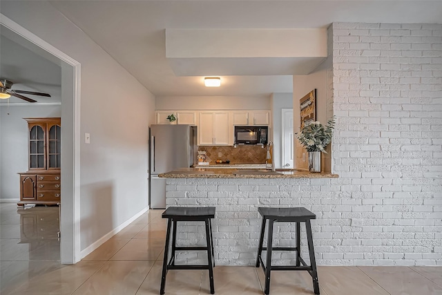 kitchen featuring freestanding refrigerator, light tile patterned flooring, a sink, white cabinets, and black microwave