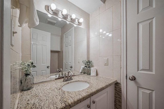 bathroom featuring visible vents, decorative backsplash, tile walls, and vanity