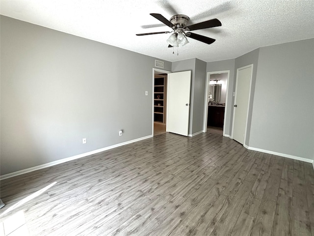 unfurnished bedroom with dark wood finished floors, a textured ceiling, baseboards, and ensuite bathroom