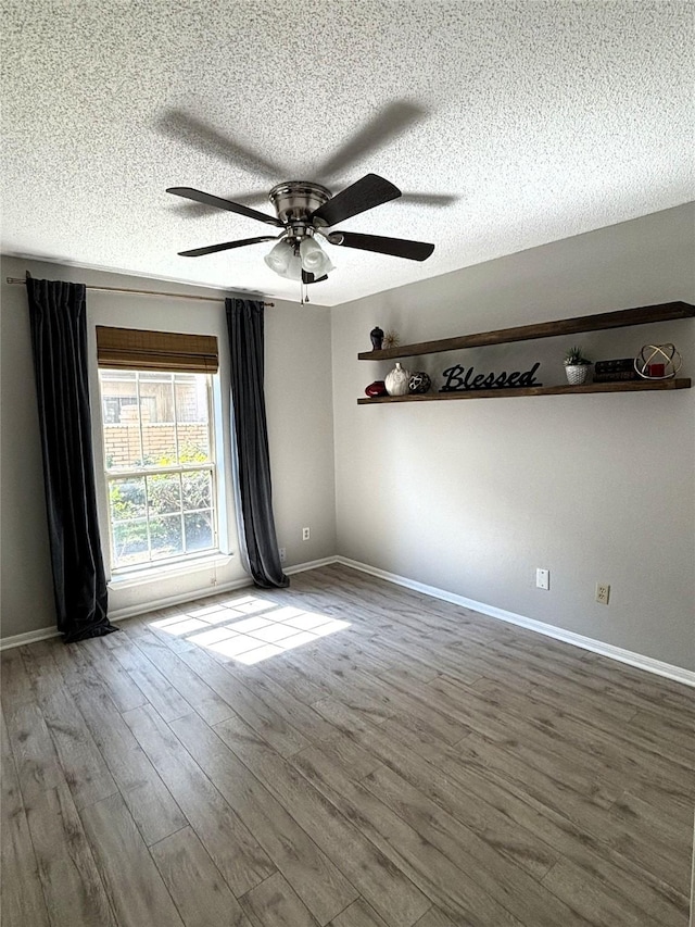 spare room featuring a textured ceiling, wood finished floors, a ceiling fan, and baseboards