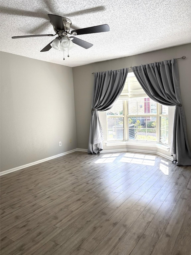 spare room with a textured ceiling, ceiling fan, wood finished floors, and baseboards