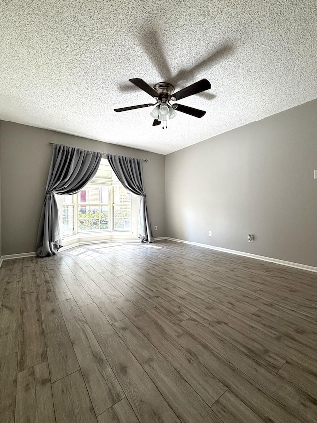 unfurnished room featuring a textured ceiling, dark wood-style flooring, a ceiling fan, and baseboards