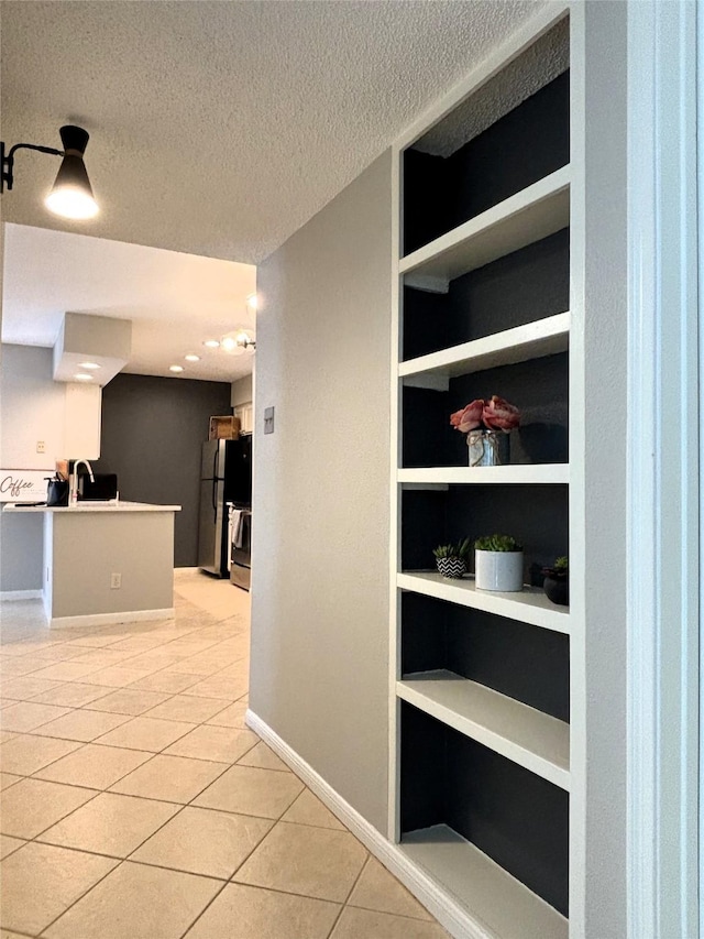 interior space featuring built in features, light tile patterned floors, a sink, a textured ceiling, and baseboards