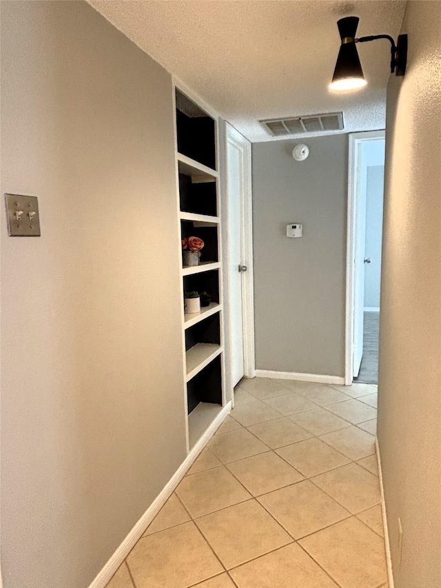 hall featuring light tile patterned floors, built in shelves, baseboards, and a textured ceiling