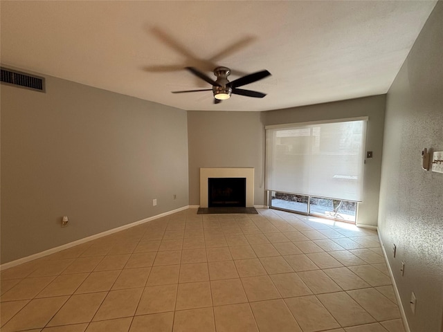 unfurnished living room with a fireplace with raised hearth, light tile patterned flooring, a ceiling fan, visible vents, and baseboards